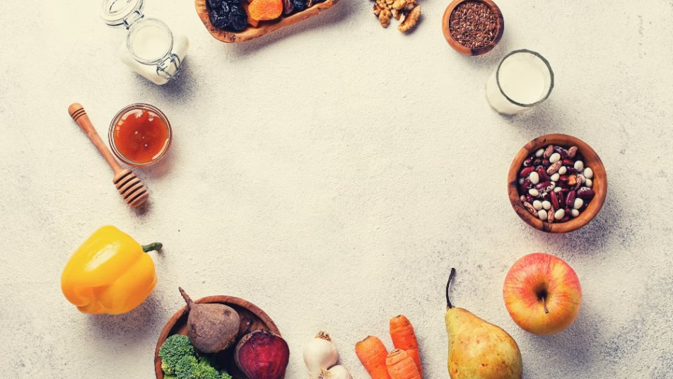 na jasnym blacie leżą ułożone w kole produkty spożywcze takie jak owoce, warzywa, miód, orzechy i nabiał