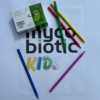 kartka z napisem Mycobiotic KIDS, obok produkt Mycobiotic KIDS, w tle kolorowe kredki