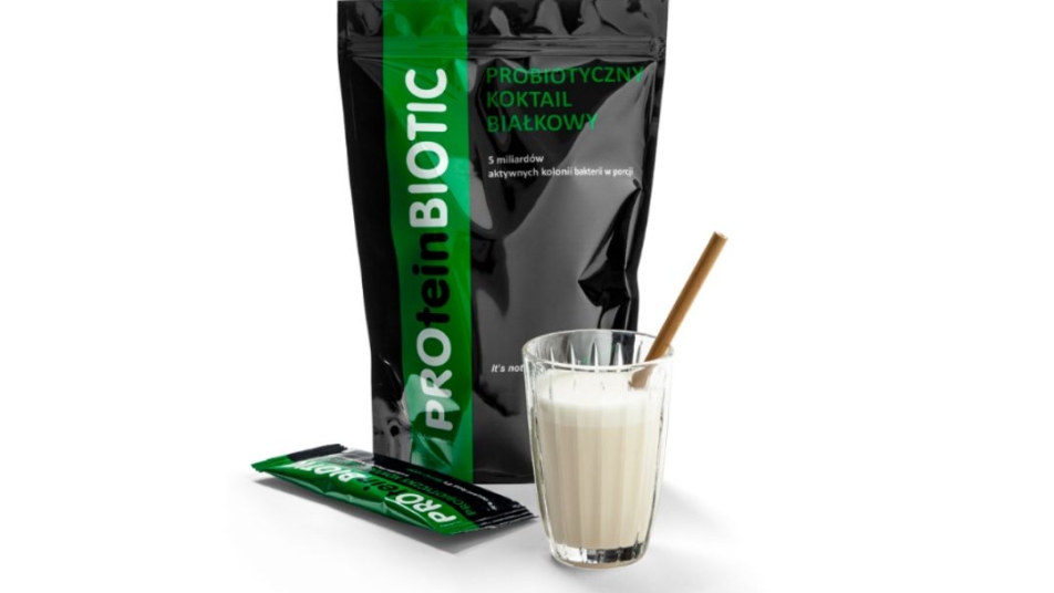 Opakowanie produktu PROteinBIOTIC, obok szklanka z białym koktajlem i słomką, a także mała, pojedyncza saszetka produktu