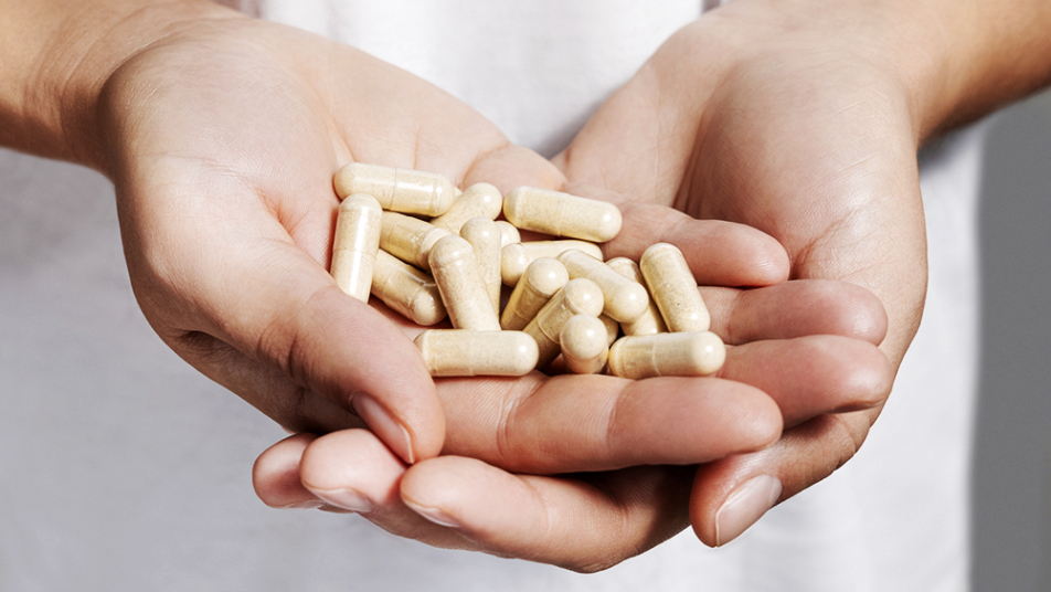 Dwie dłonie trzymające garść kapsułek probiotyków.